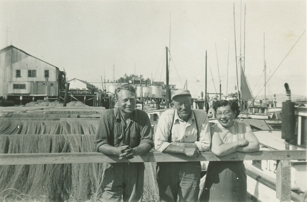 Two men and a woman in front of fishing nets at in front of harbour
